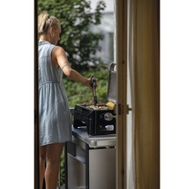 Frau grillt Würstchen und Gemüse auf einem Tischgrill im Freien.