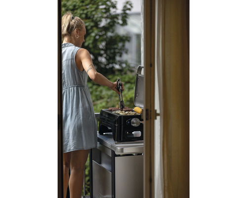 Frau grillt Würstchen und Gemüse auf einem Tischgrill im Freien.