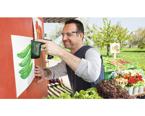 Ein Mann befestigt mit einem Akku-Tacker ein Blatt Papier an einer Verkaufstheke für Gemüse.