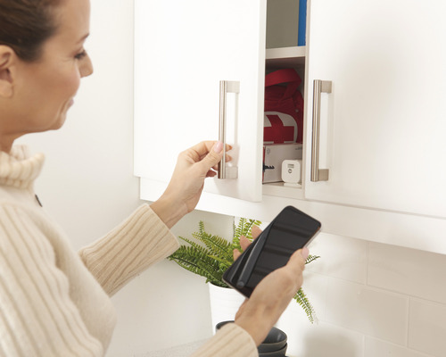 Frau öffnet weißen Küchenschrank mit Smartphone in der Hand