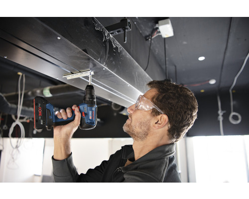 Un homme travaille sur une structure de plafond avec une perceuse-visseuse sans fil.