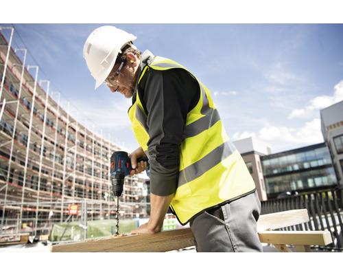 Un artisan perce un trou dans une planche de bois avec une perceuse.
