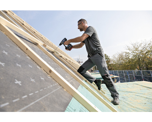 Un artisan fixe des liteaux de toiture à l'aide d'une visseuse sans fil sur une structure de toit.