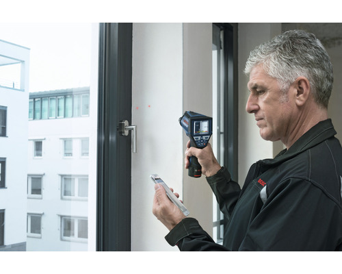 Un homme utilise une caméra thermique pour analyser une fenêtre.