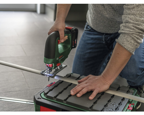 Une personne coupe un tube avec une scie sauteuse sans fil sur une table de sciage.
