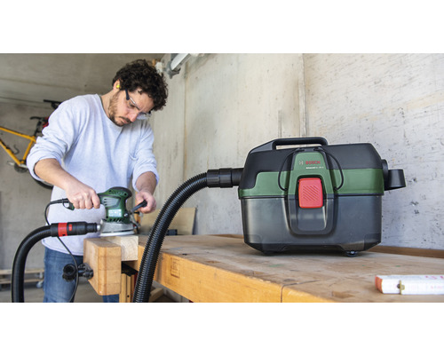 Artisan ponçant avec une ponceuse et un aspirateur Bosch sur un établi.