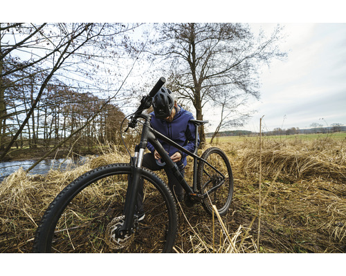 Mann mit Helm repariert ein Mountainbike in der Natur.