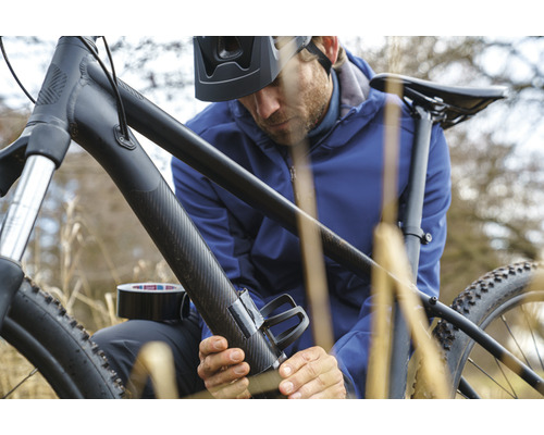 Mann befestigt Flaschenhalter mit Klebeband an einem Fahrrad
