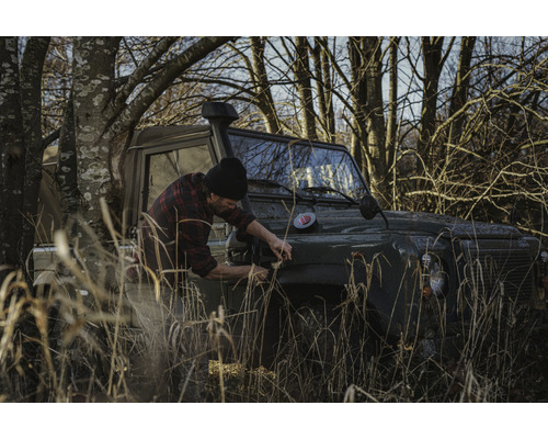 Mann öffnet die Motorhaube eines Geländewagens in der Natur
