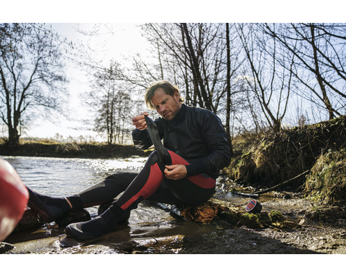 Mann zieht Neoprensocken am Wasser an