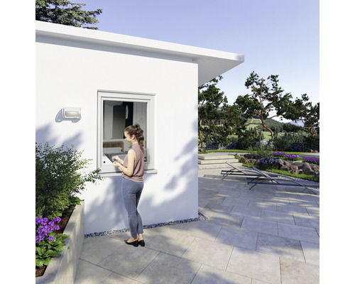 Frau steht vor einem Gartenhaus mit Kunststofffenster und geniesst den Blick in den Garten.