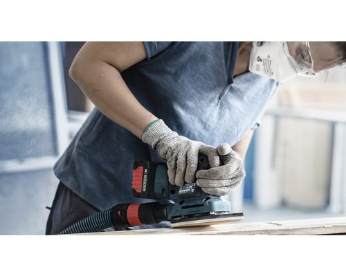 Une personne ponce du bois avec une ponceuse vibrante sans fil, portant des gants de protection et un masque antipoussière.