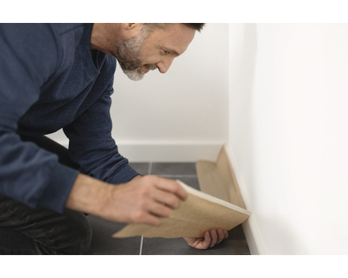Handwerker verlegt eine Schutzfolie entlang einer Wand auf einem Fliesenboden.