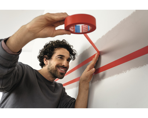 Un homme colle du ruban adhésif rouge sur un mur pour la peinture décorative.