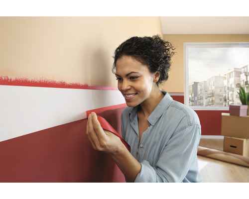 Femme retirant du ruban de masquage d''un mur peint.