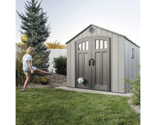 Remise à outils LIFETIME Jupiter avec plancher et étagère 243 x 304 cm gris Scène de jardin avec abri de jardin et jeune fille jouant au football