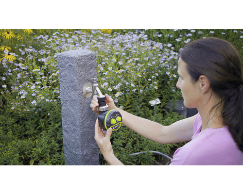 Une femme fixe une horloge d''arrosage sur un robinet dans le jardin.