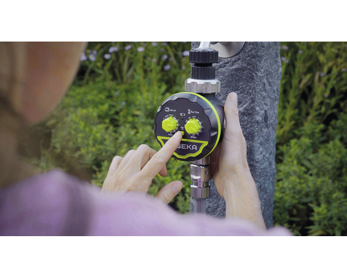 Une personne règle un ordinateur d''arrosage de la marque SEKA sur un robinet.
