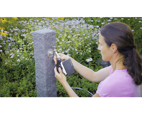 Une femme installe un ordinateur d''arrosage sur un robinet de jardin.