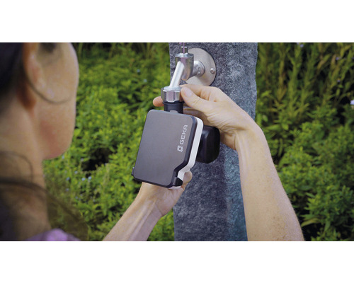 Une personne fixe un programmateur d''arrosage Geka sur un robinet de jardin.