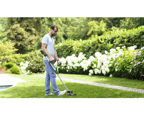 Un homme portant des lunettes de sécurité coupe du gazon avec un coupe-bordure dans un jardin.
