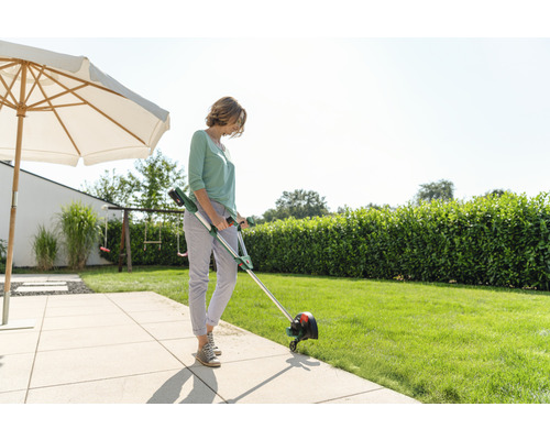 Une femme coupe l'herbe avec un coupe-bordures à batterie dans le jardin.