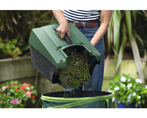 Une personne vide l'herbe et les feuilles dans un sac de jardin à l'aide d'une balayeuse
