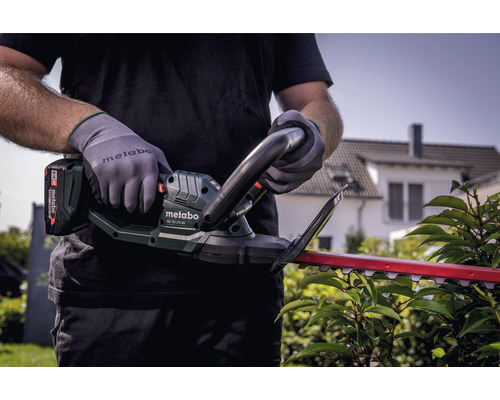 Une personne utilise un taille-haie à batterie Metabo pour tailler une haie
