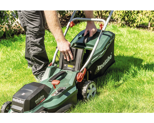 Un homme insère une batterie dans une tondeuse à gazon Metabo