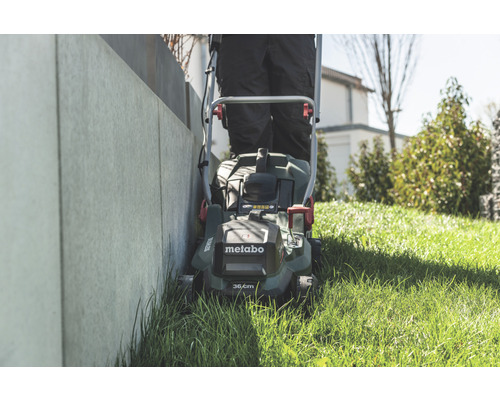 Une personne tond le gazon avec une tondeuse à gazon Metabo le long d''un mur.