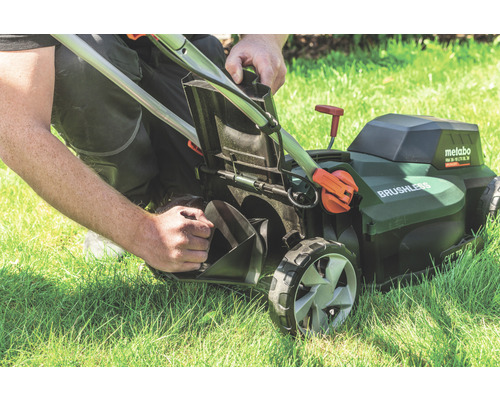 Un homme vide le bac de ramassage d''une tondeuse à gazon sans fil Metabo sur une pelouse.