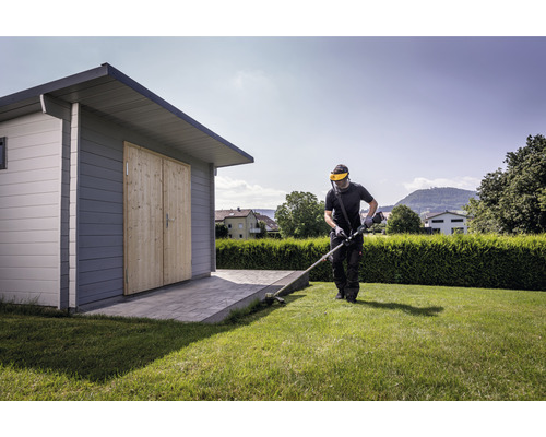 Un homme coupe du gazon avec un coupe-bordures à côté d''un abri de jardin.