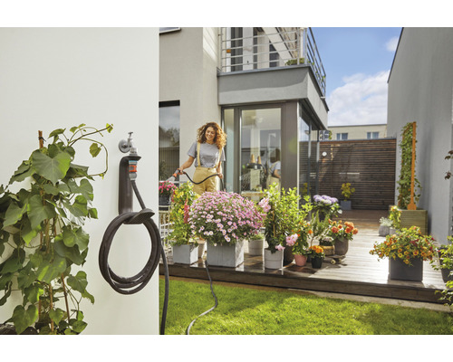 Une femme arrose des fleurs avec un tuyau d''arrosage dans le jardin avec support de tuyau