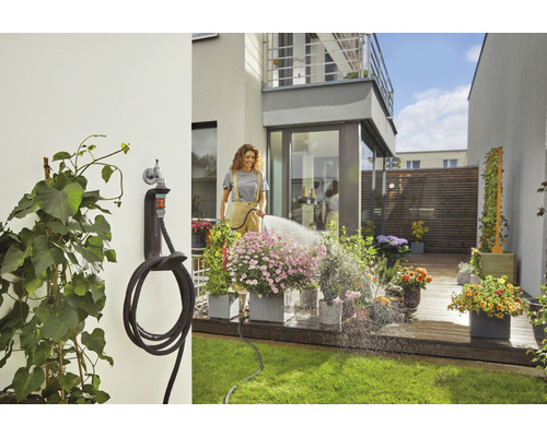 Femme arrosant des fleurs avec un tuyau d''arrosage sur une terrasse