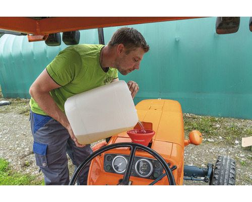 Un homme verse du liquide dans un tracteur à l''aide d''un entonnoir