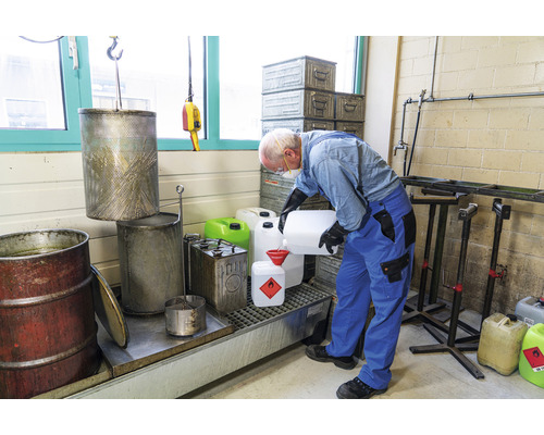 Une personne en équipement de protection verse du liquide dans un récipient avec un marquage de marchandises dangereuses.