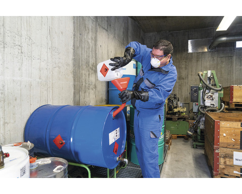 Une personne verse du liquide dans un fût, portant des vêtements de protection.