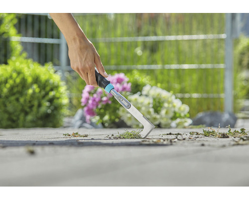 Nahaufnahme einer Person, die mit einem Fugenkratzer Unkraut entfernt
