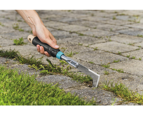 Person entfernt Unkraut mit einem Fugenkratzer zwischen Pflastersteinen.