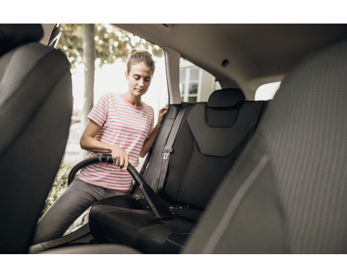 Une femme aspire les sièges de voiture avec un aspirateur.