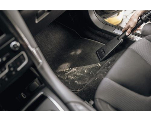 Une personne aspire l''espace pour les pieds sale d''une voiture avec un aspirateur.