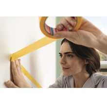 Frau bringt Malerband an der Wand an