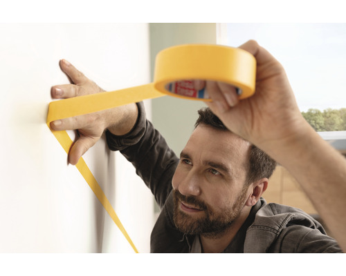 Mann befestigt Malerkrepp an einer Wand