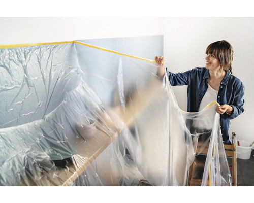 Une femme recouvre des meubles de film de protection pour les protéger des éclaboussures de peinture.