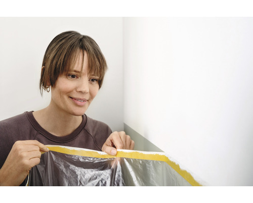 Femme fixant un film de protection avec du ruban adhésif sur un mur avant de peindre