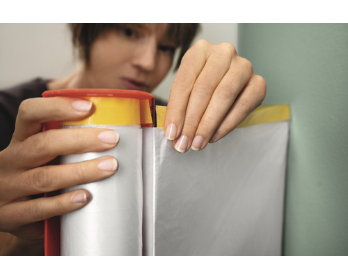 Femme fixant du ruban de masquage et un film de protection sur un mur.
