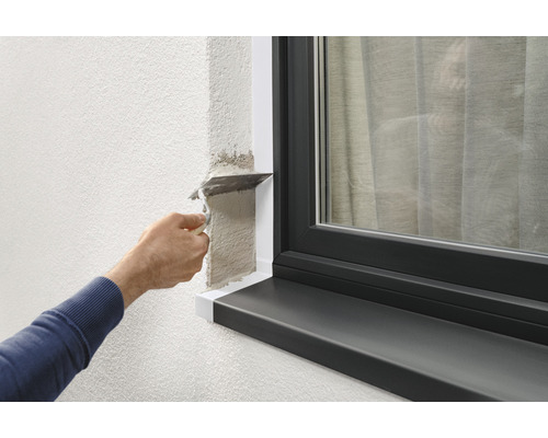 Handwerker trägt Spachtelmasse auf Wand neben Fenster auf