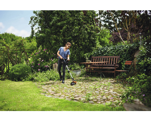 Une femme utilise un coupe-bordures dans un jardin verdoyant avec des fleurs et des arbres