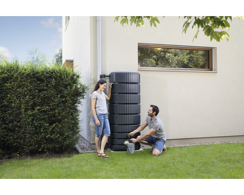 Szene mit einer Regentonne, die an einer Hauswand steht und von zwei Personen bedient wird.