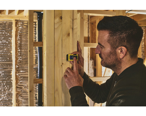 Un homme utilise un télémètre numérique Stanley sur un mur en bois